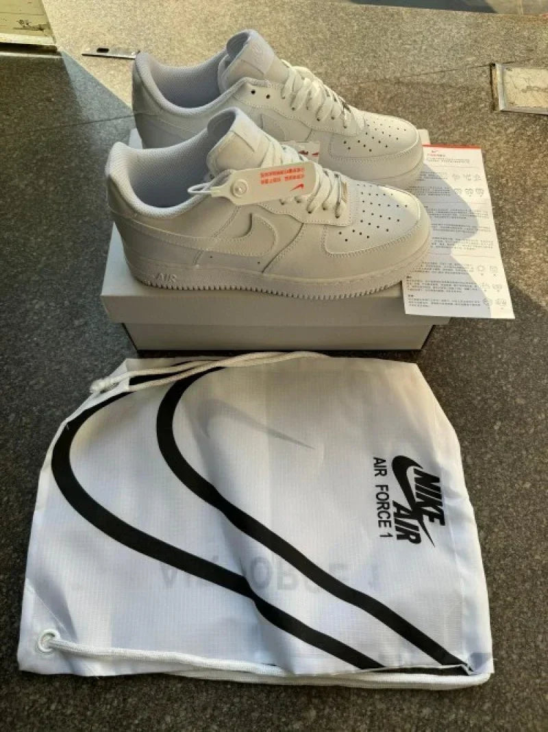 Pair of white Nike Air Force 1 sneakers on a box with branded dust bag and paperwork.
