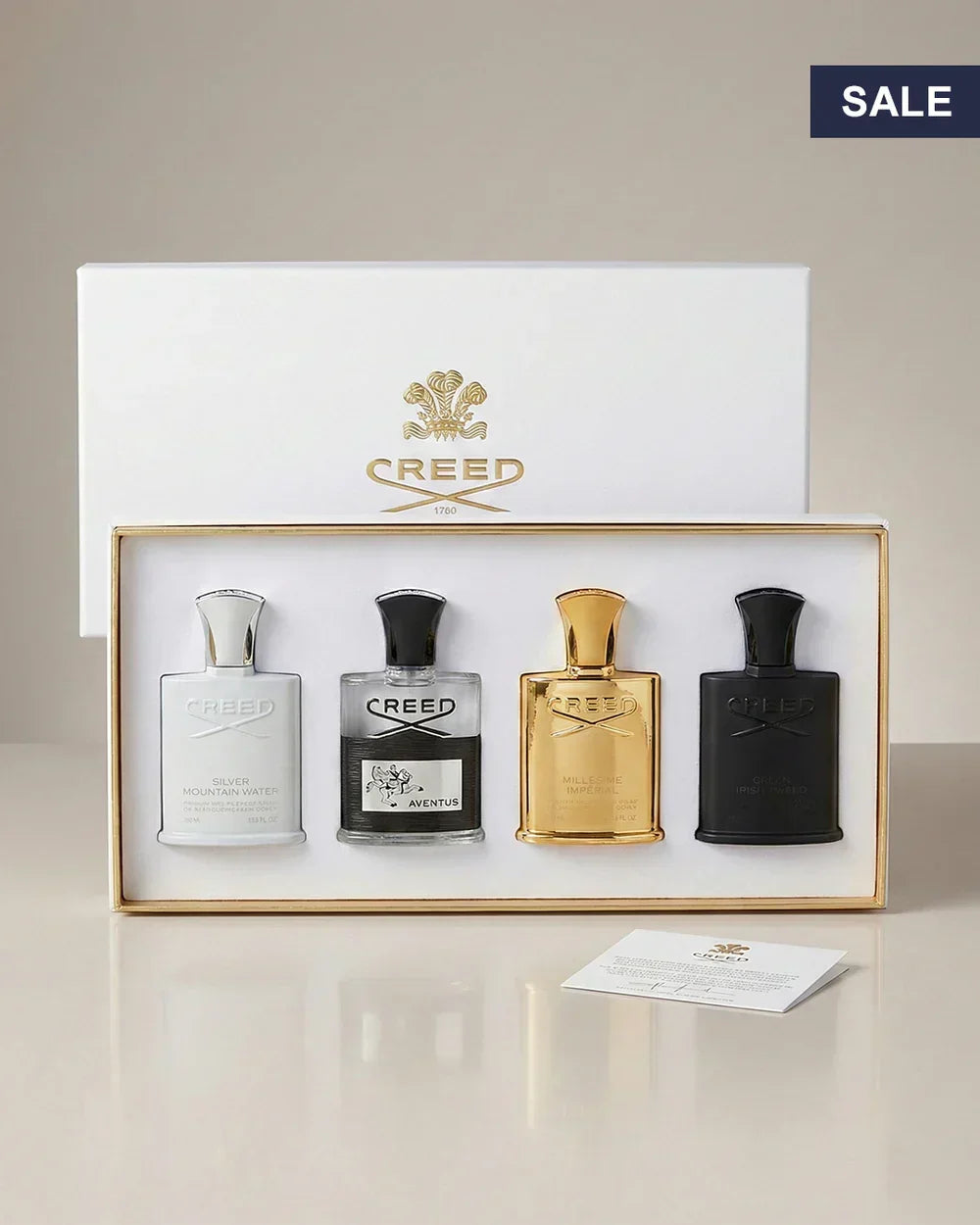 Luxury fragrance gift set with four Creed perfume bottles in white, black, silver, and gold packaging.